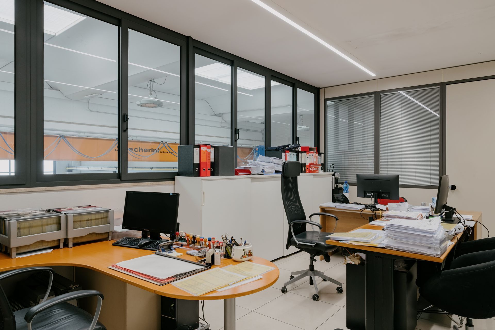 Modern office with desks, computers, chairs, and large windows overlooking an industrial area
