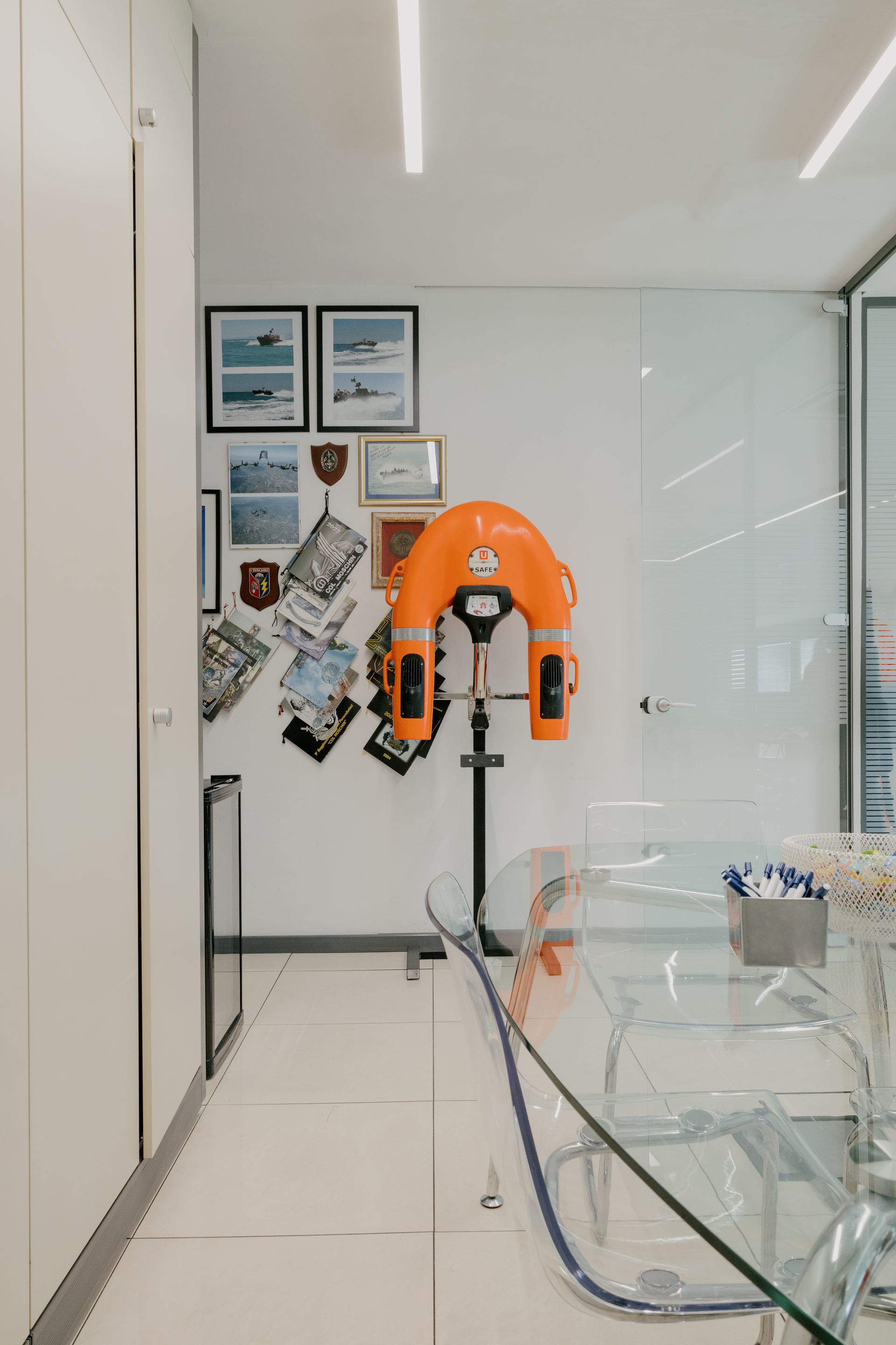 Orange robot in a bright office hallway with framed wall art and glass desks.