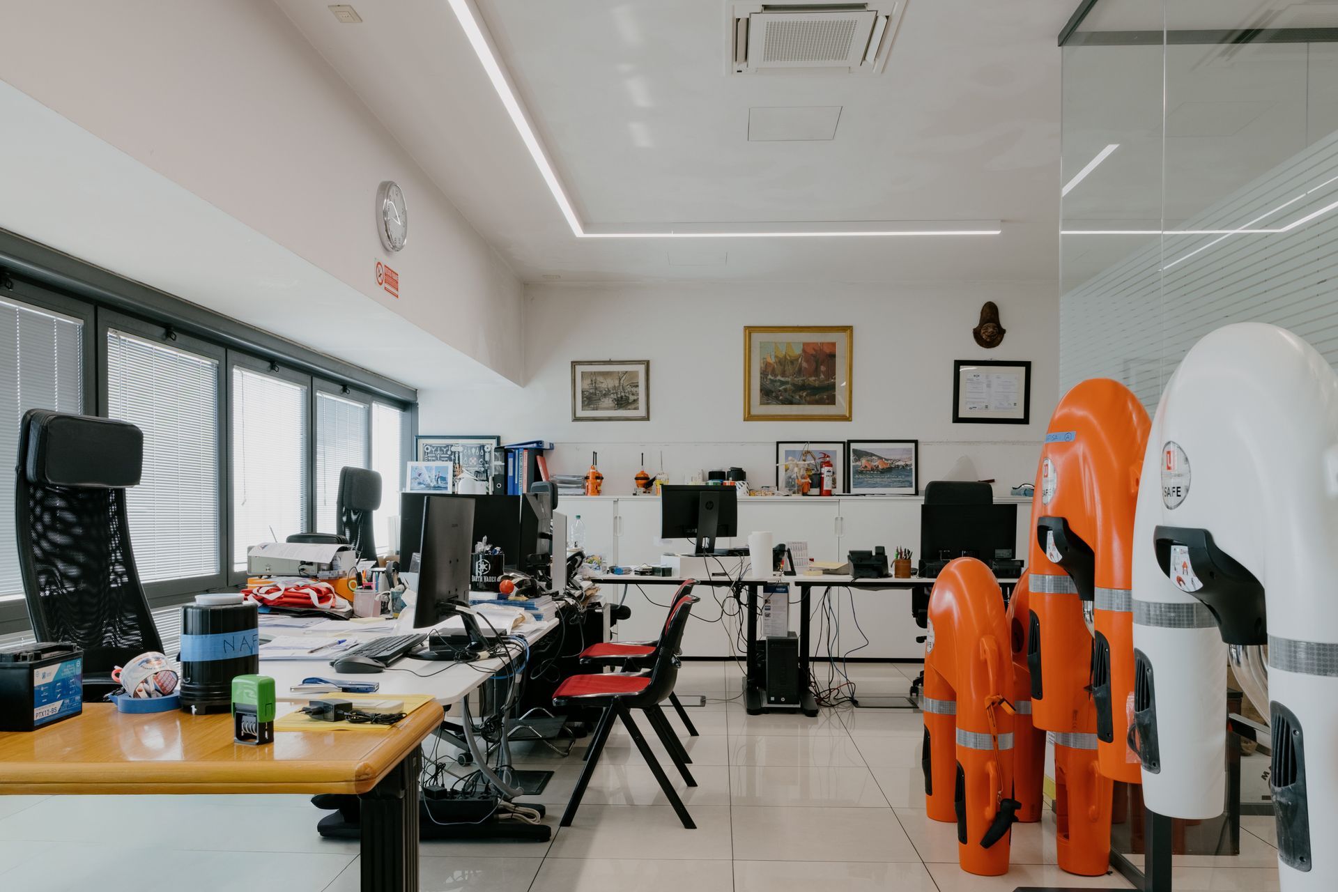 Modern office with desks, computer monitors, orange safety vests, and wall art