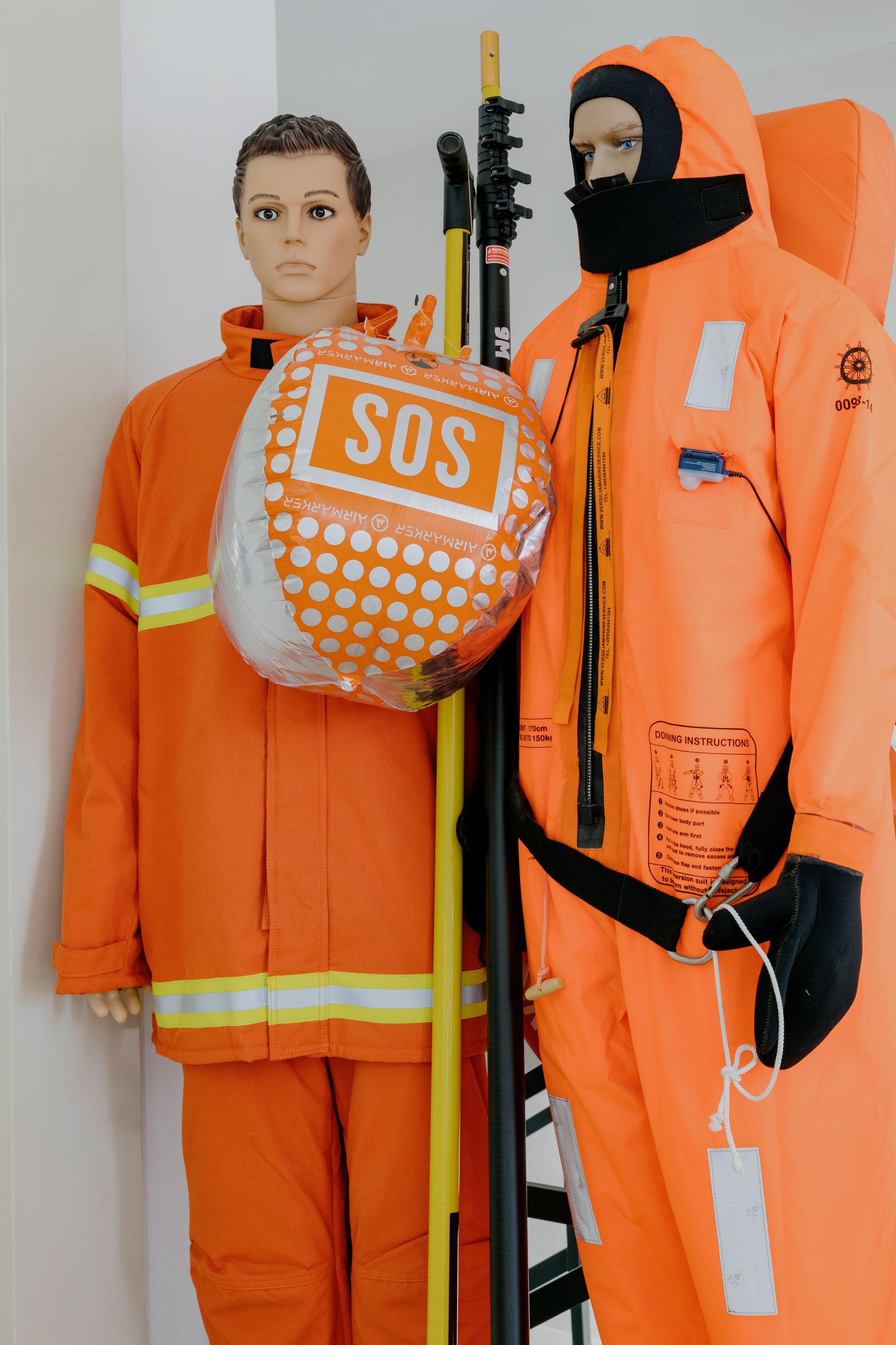 Orange rescue suits with SOS life preserver and mannequin display indoors