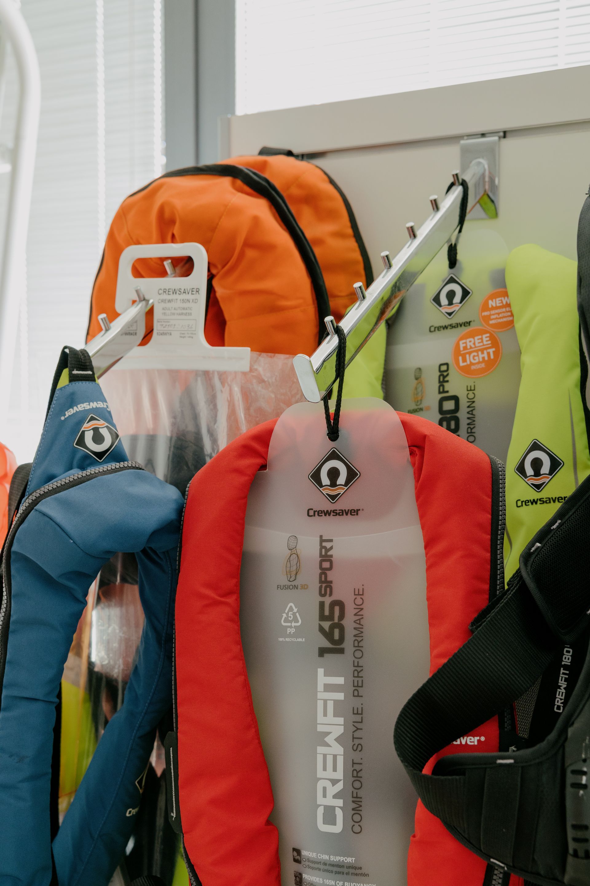 Colorful life jackets hanging indoors on a rack by a window