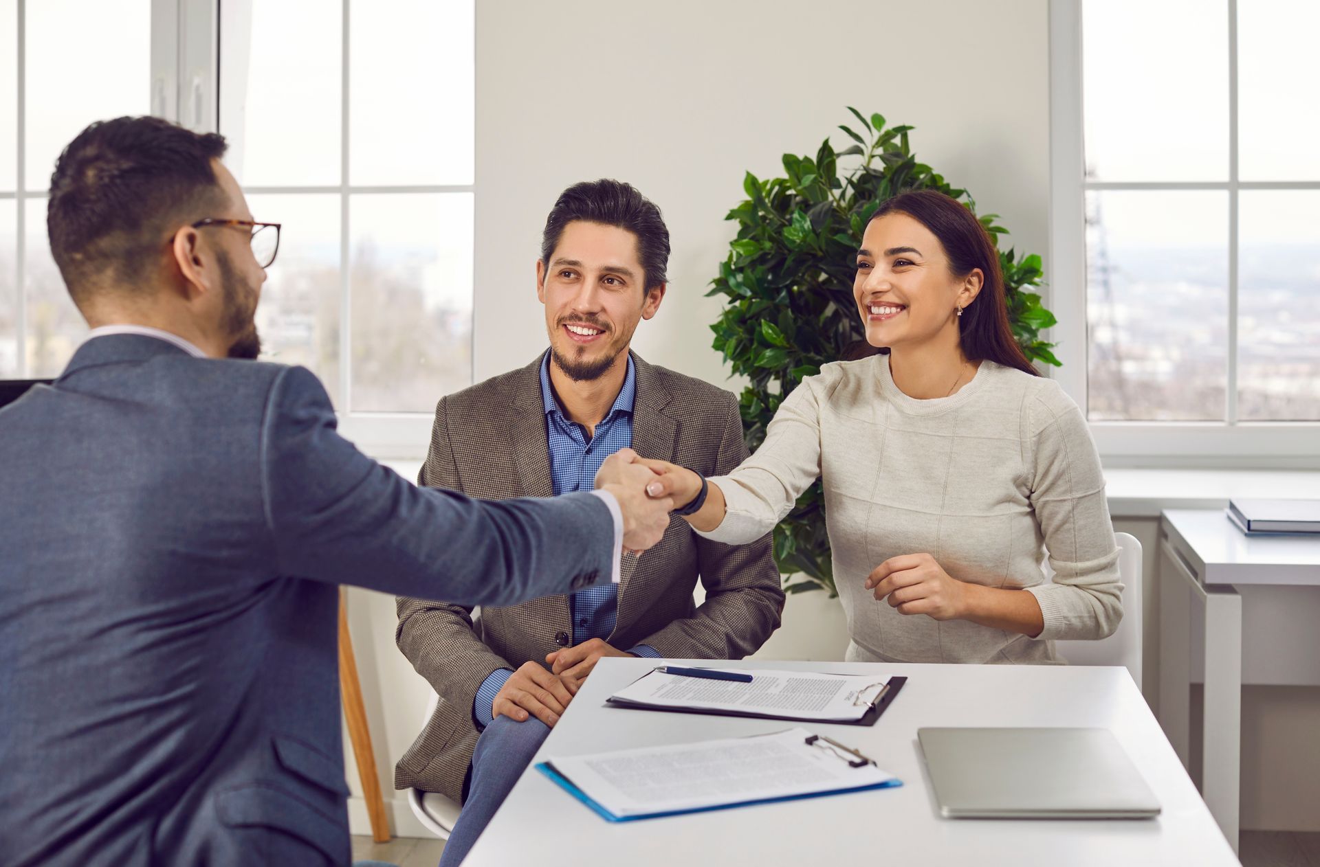 A couple fist-bumps a professional at a table, likely after a deal. White room, papers, laptop.