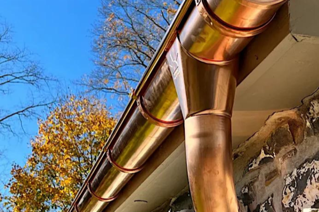 A close up of a copper gutter on a roof with trees in the background.