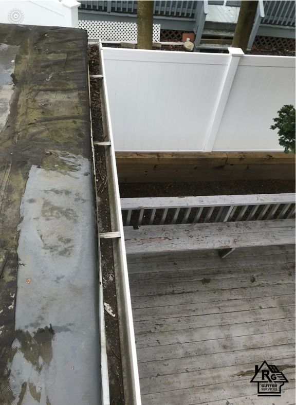 A gutter on a deck with a white fence in the background.