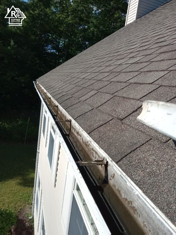 A gutter on the side of a house with a roof in the background.