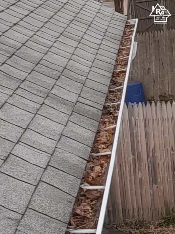 A gutter filled with leaves on a roof next to a wooden fence.