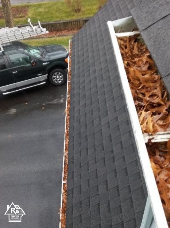 A black suv is parked on the side of a roof next to a gutter filled with leaves