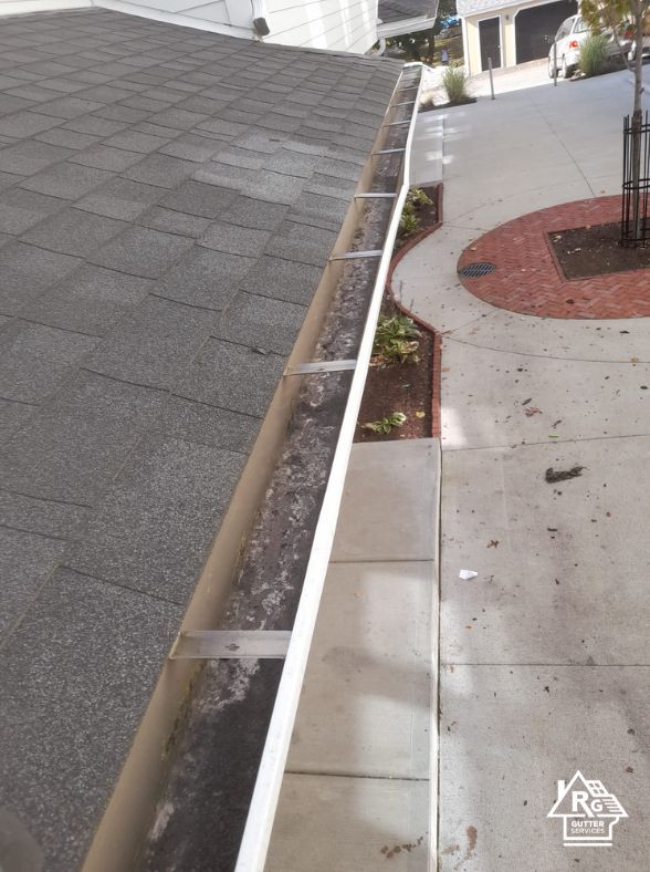 A close up of a gutter on a roof next to a sidewalk.