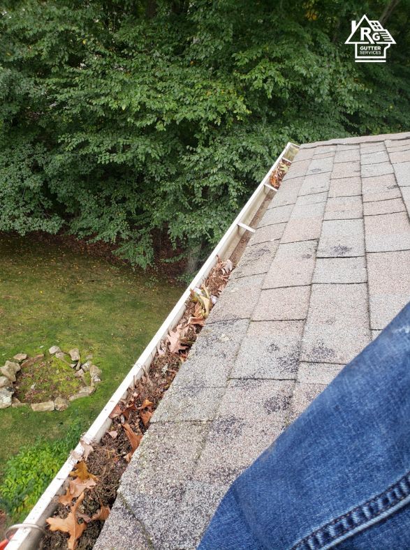 A person is standing on a roof with a gutter filled with leaves.