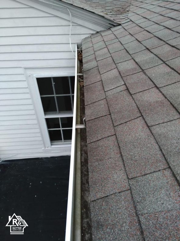 A gutter on the side of a house next to a window.