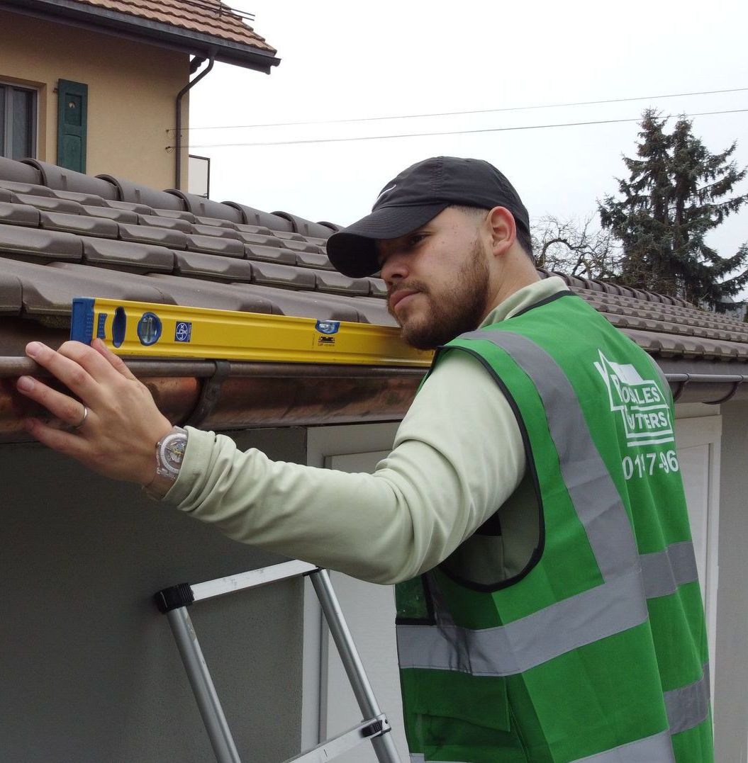 A man in a green vest is measuring a gutter with a yellow level