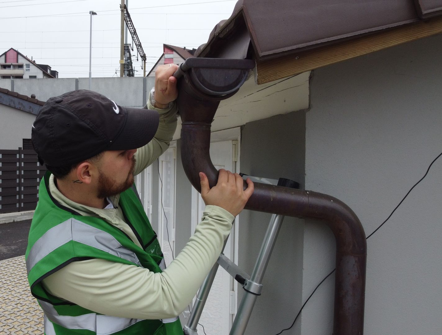 A man is fixing a gutter on the side of a building.