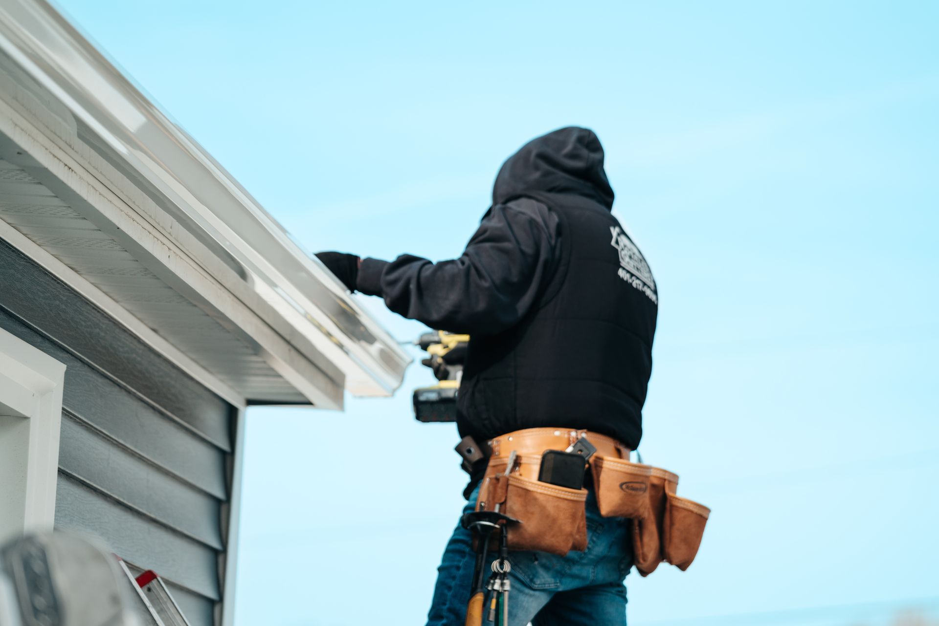 A man is standing on a ladder fixing a gutter on a house.