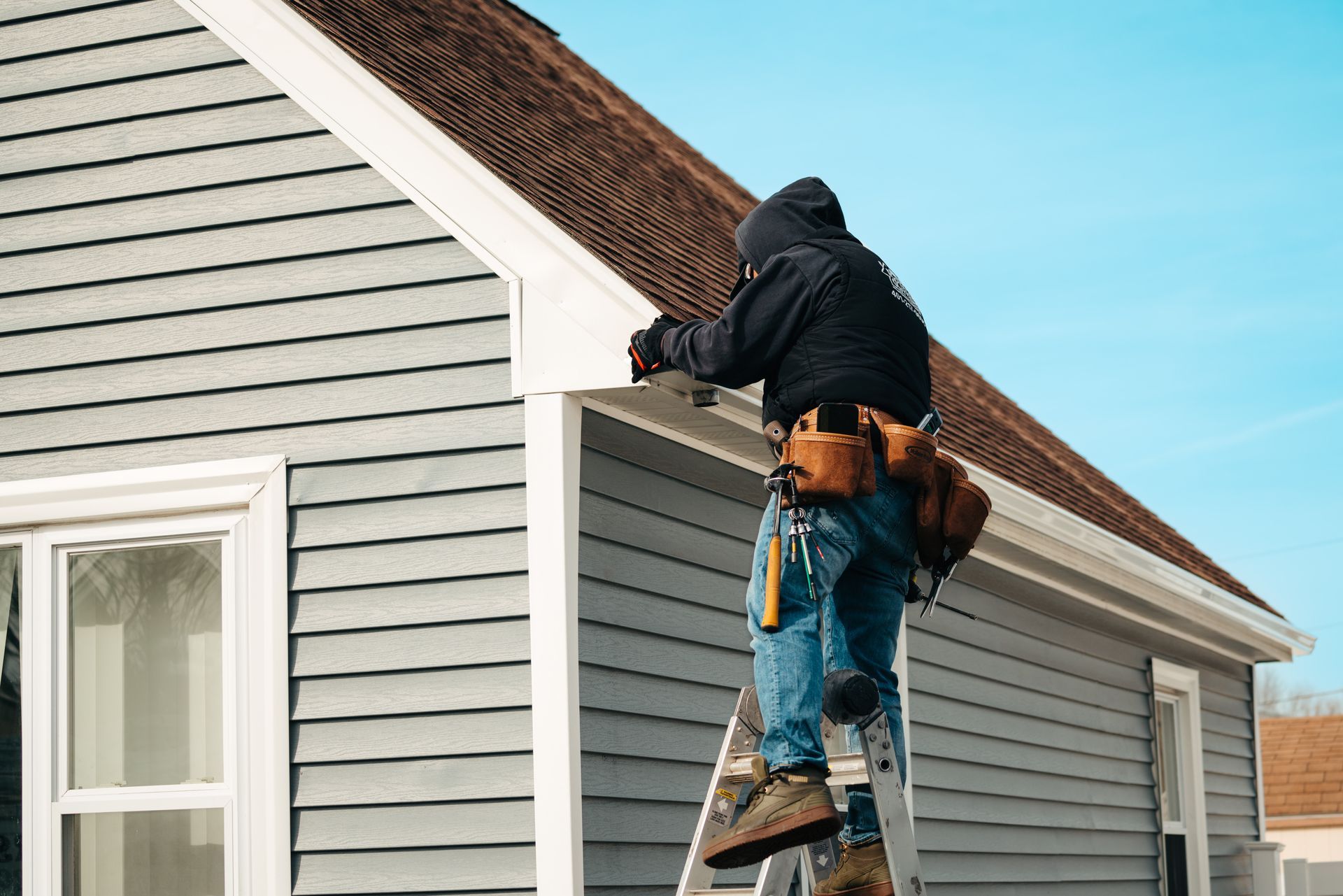 A man is standing on a ladder working on the roof of a house.