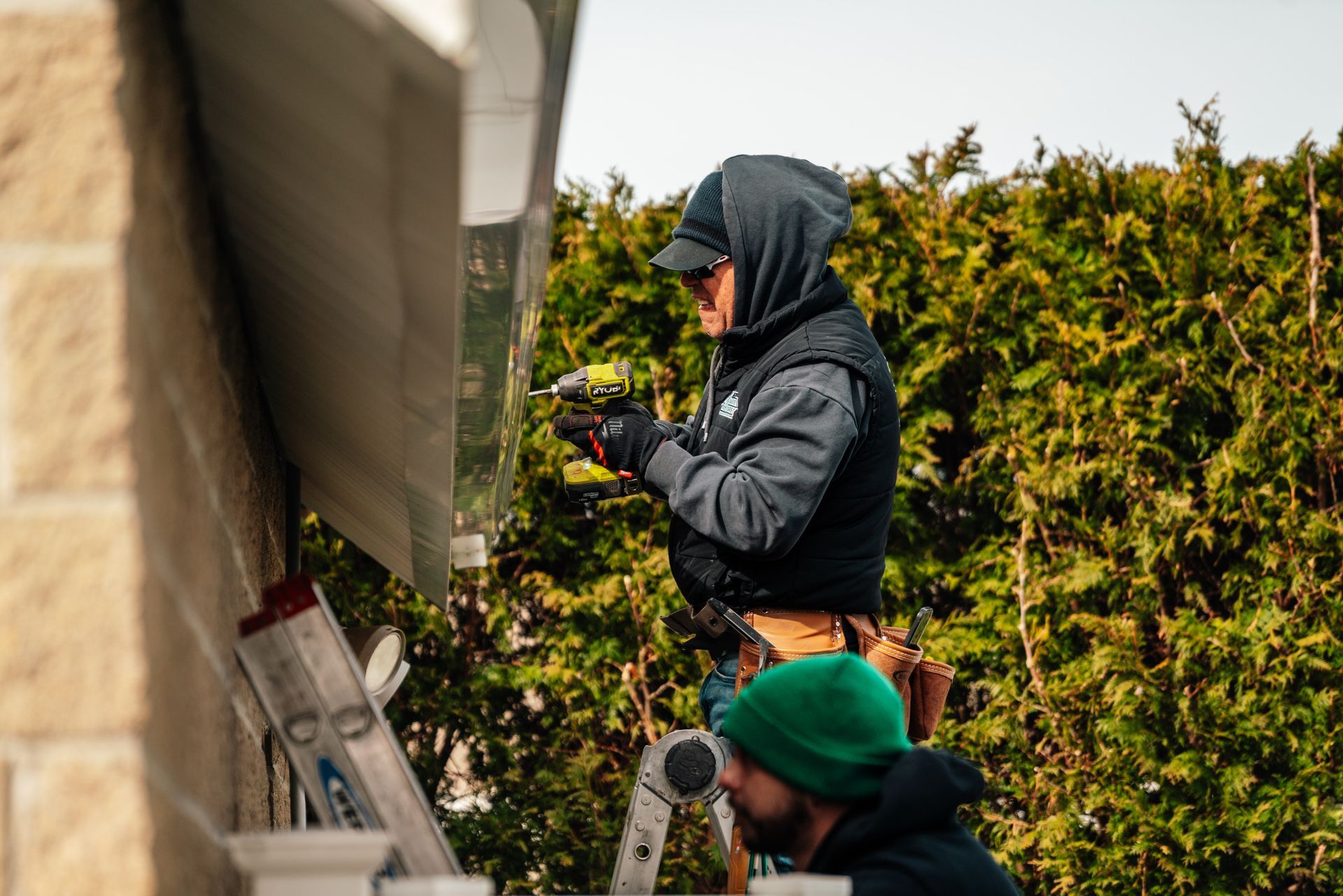 A man is using a drill to fix a gutter on a house.