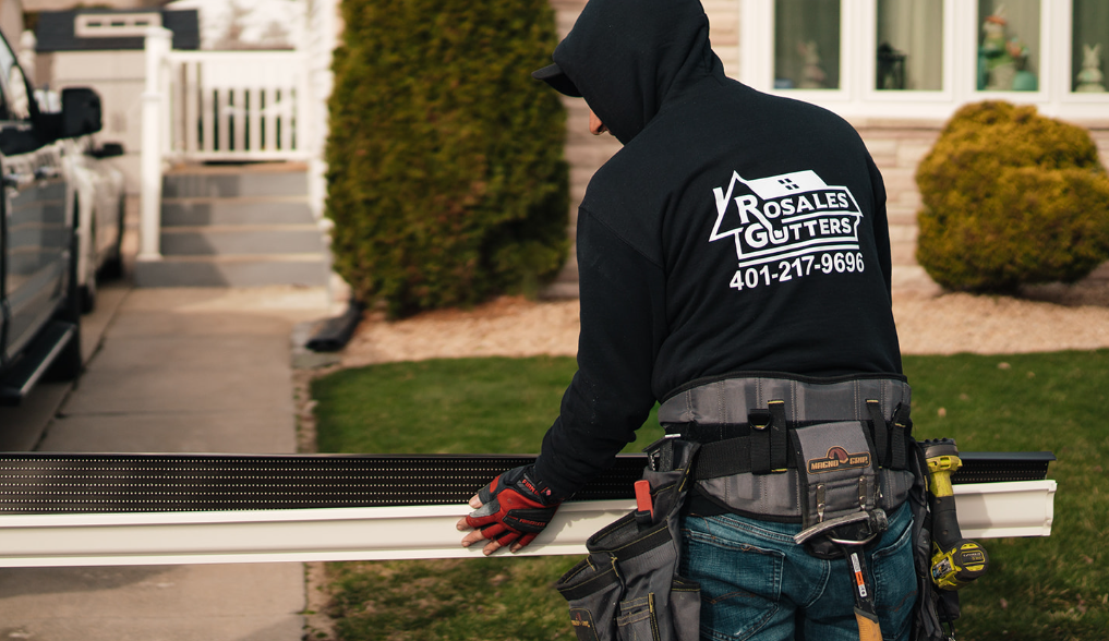 A man in a hoodie is working on a gutter in front of a house.
