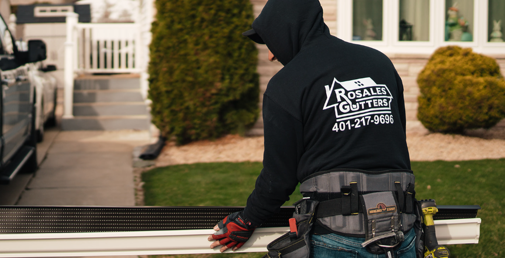 A man in a hoodie is working on a gutter in front of a house.