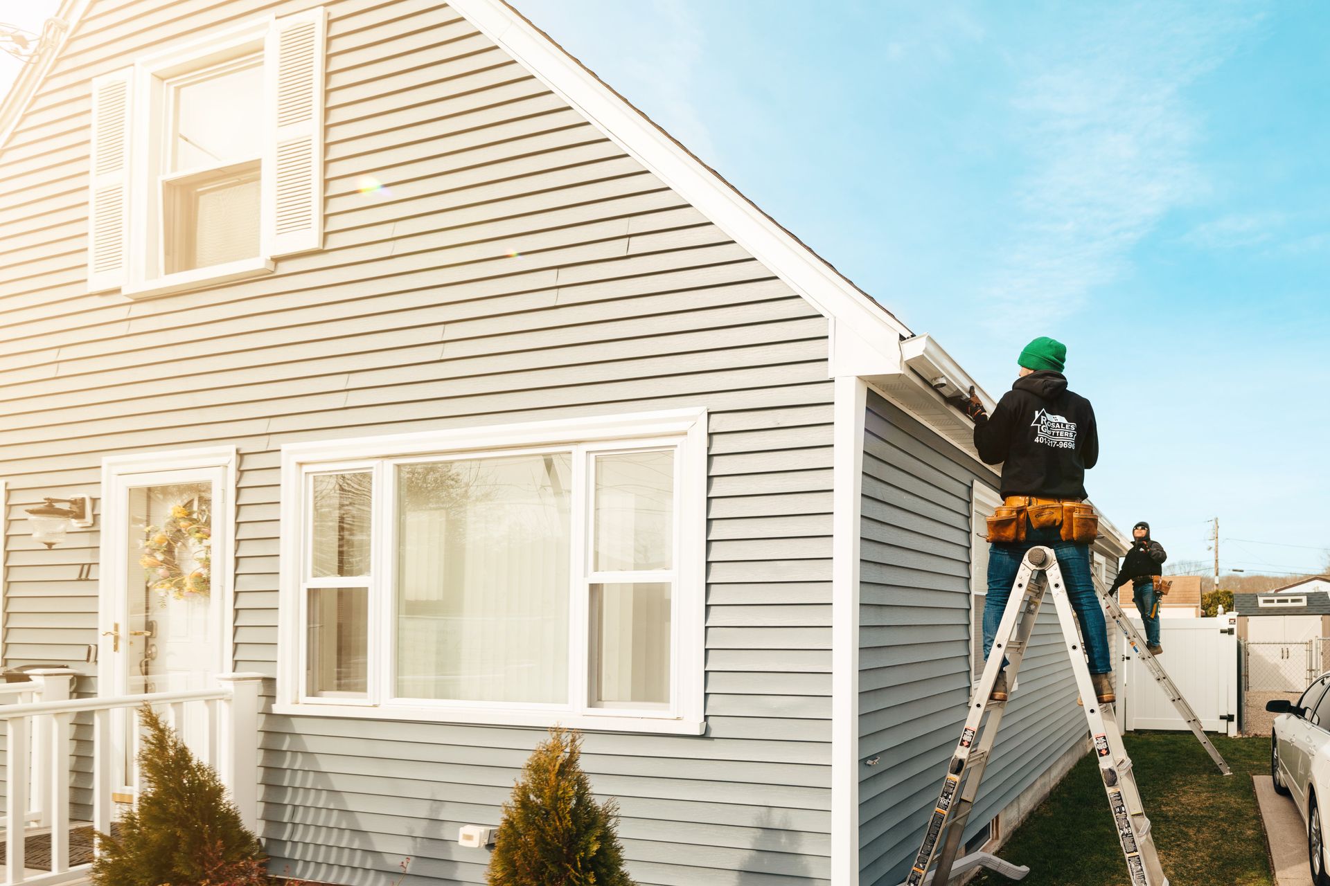 A man is standing on a ladder fixing a gutter on the side of a house.