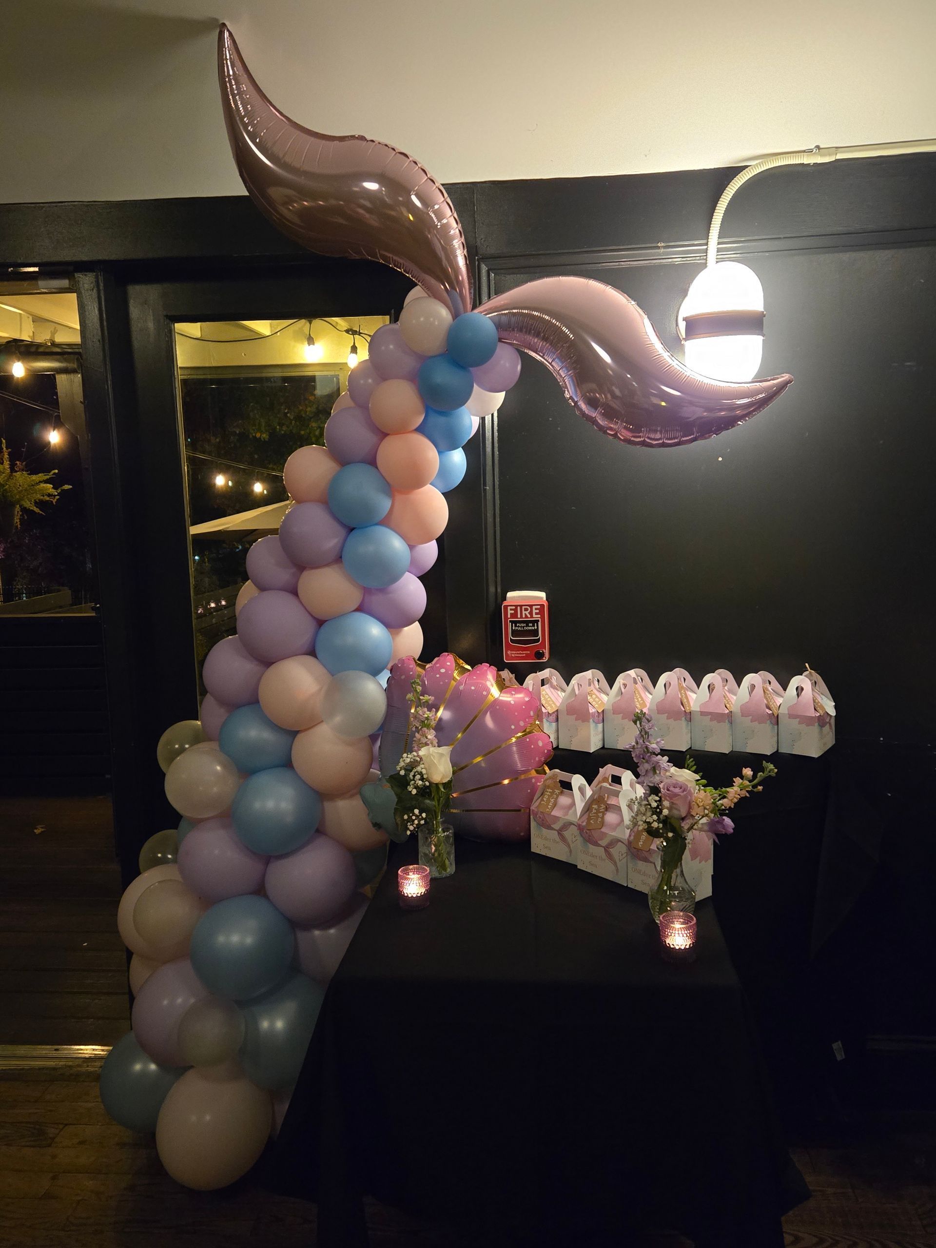 Pastel balloon arch with metallic butterfly topper beside a dessert table in a dimly lit event room