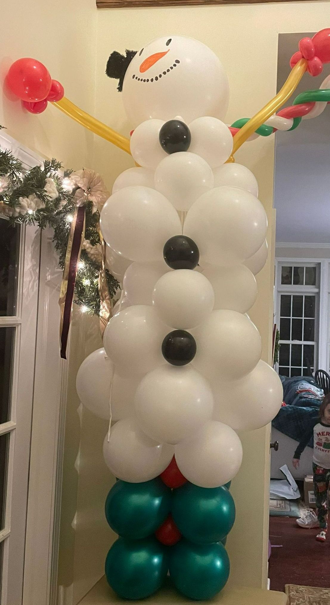 Snowman made of white and teal balloons with black buttons, standing indoors in a festive setting