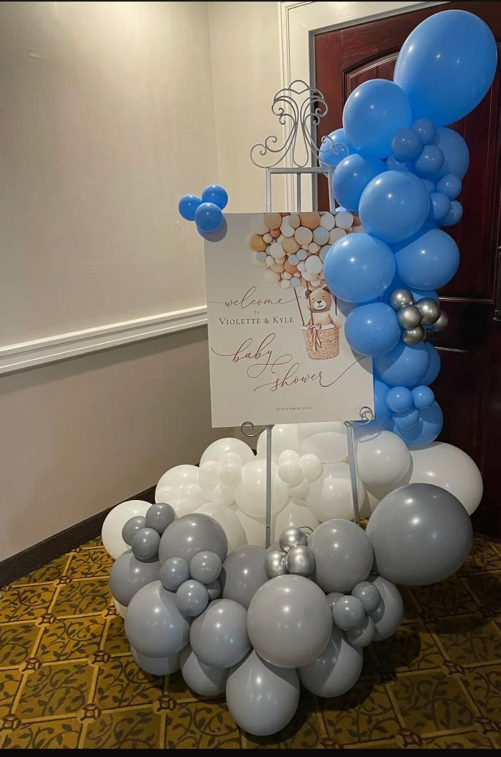 Balloon display in white, gray, and blue beside a sign in a hallway