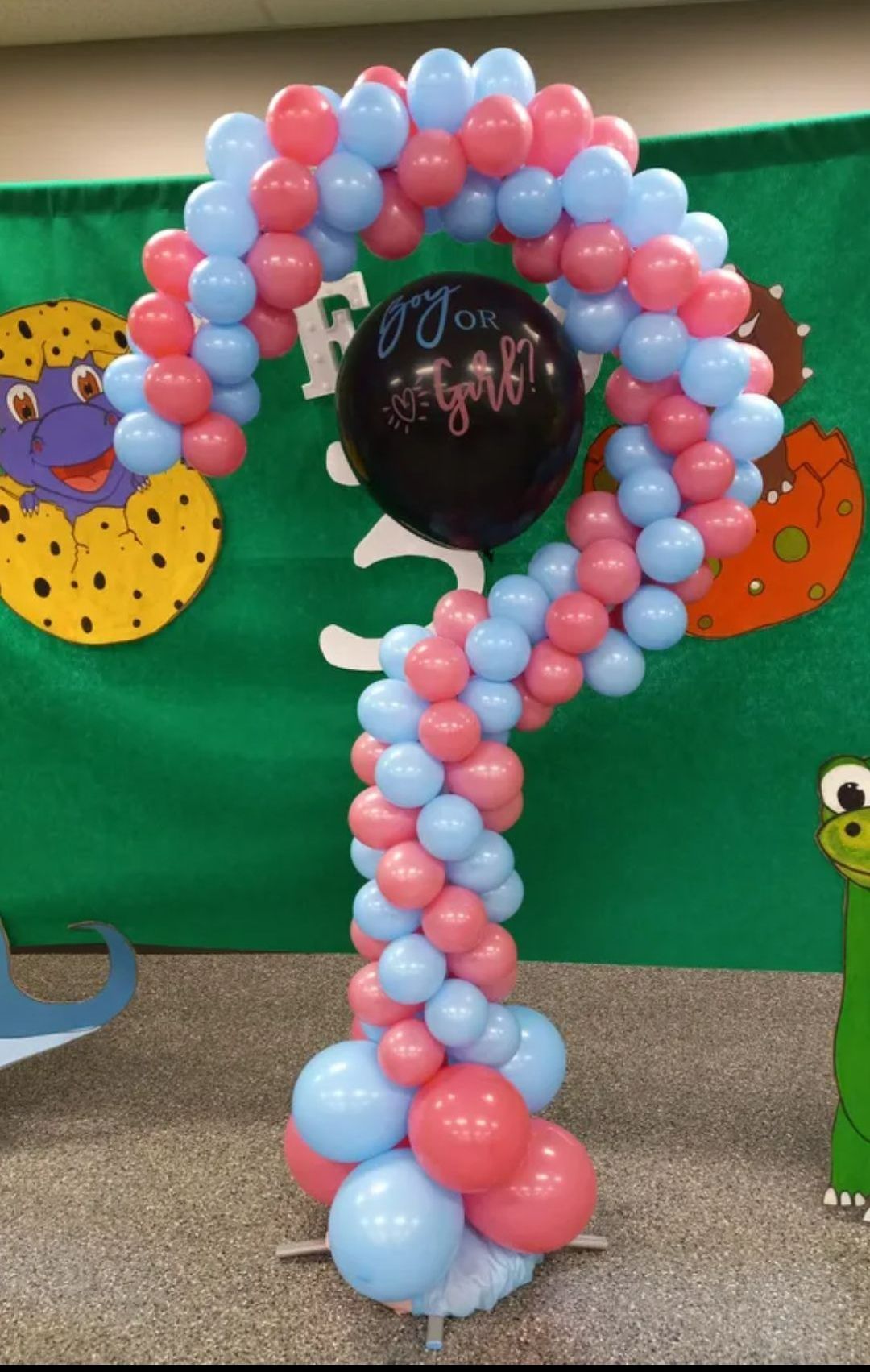 Blue and pink balloon question mark with a black sign at the center, in front of a green backdrop