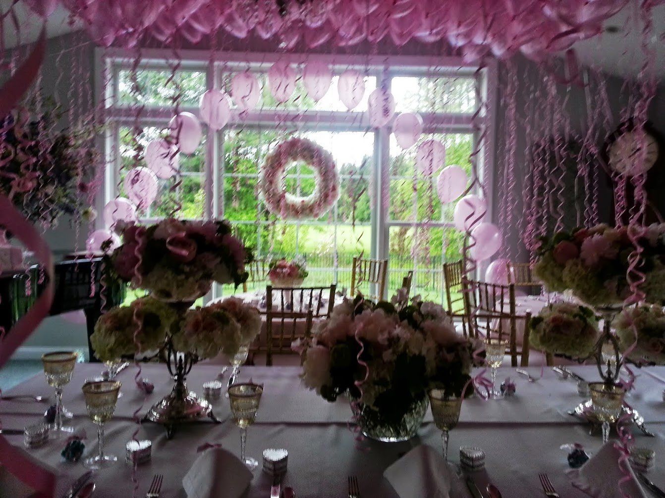 Floral-decorated banquet table in a pink-lit room with large windows and garden view