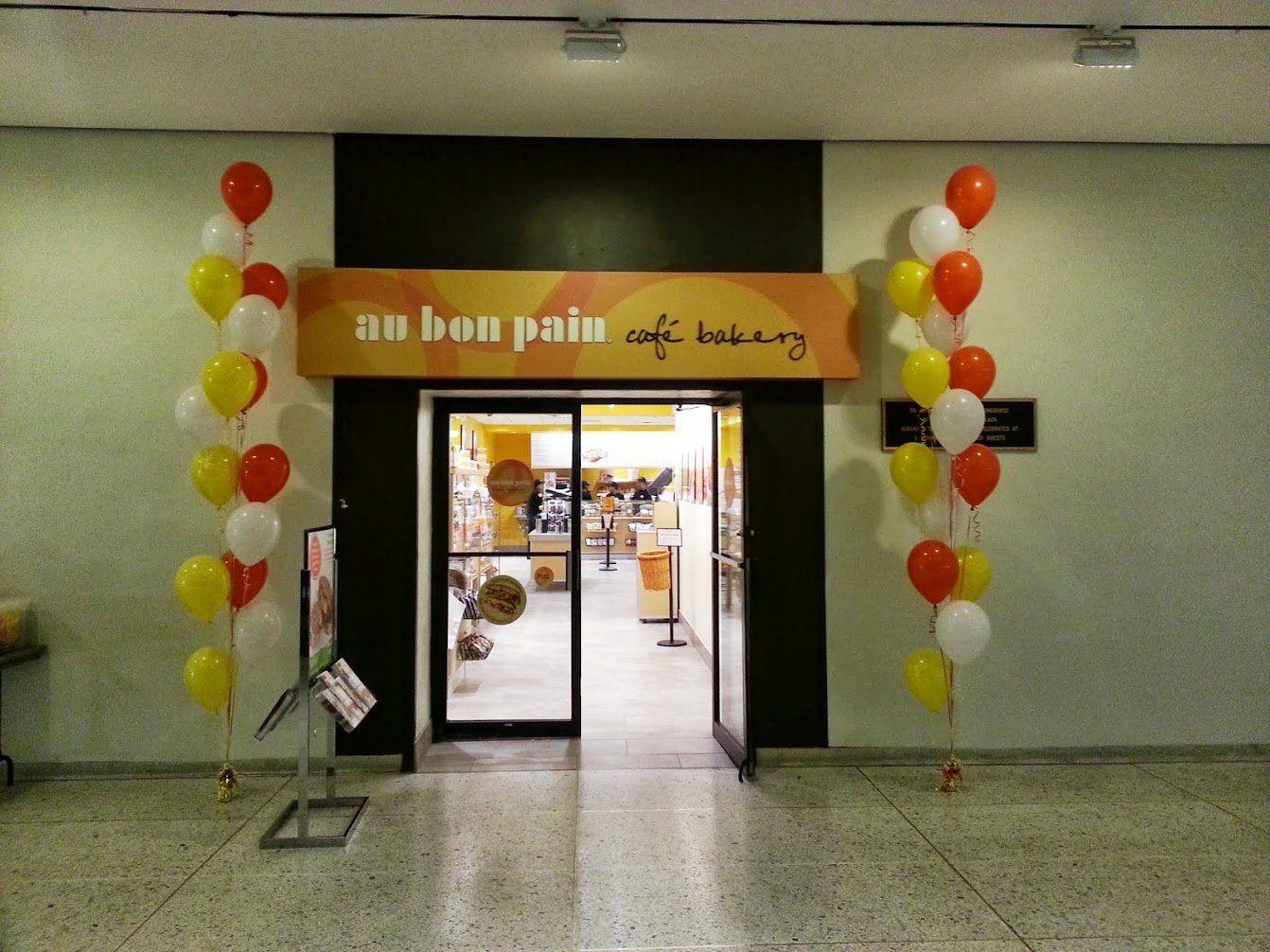 Entrance to a bakery decorated with red, yellow, and white balloons; sign reads “and then there’s cafe bakery.”