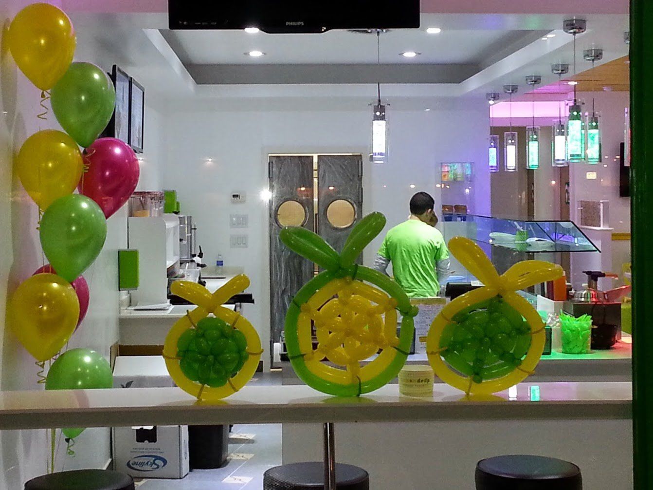Balloon decorations in a bright shop entrance, with a person in a green shirt behind the counter.