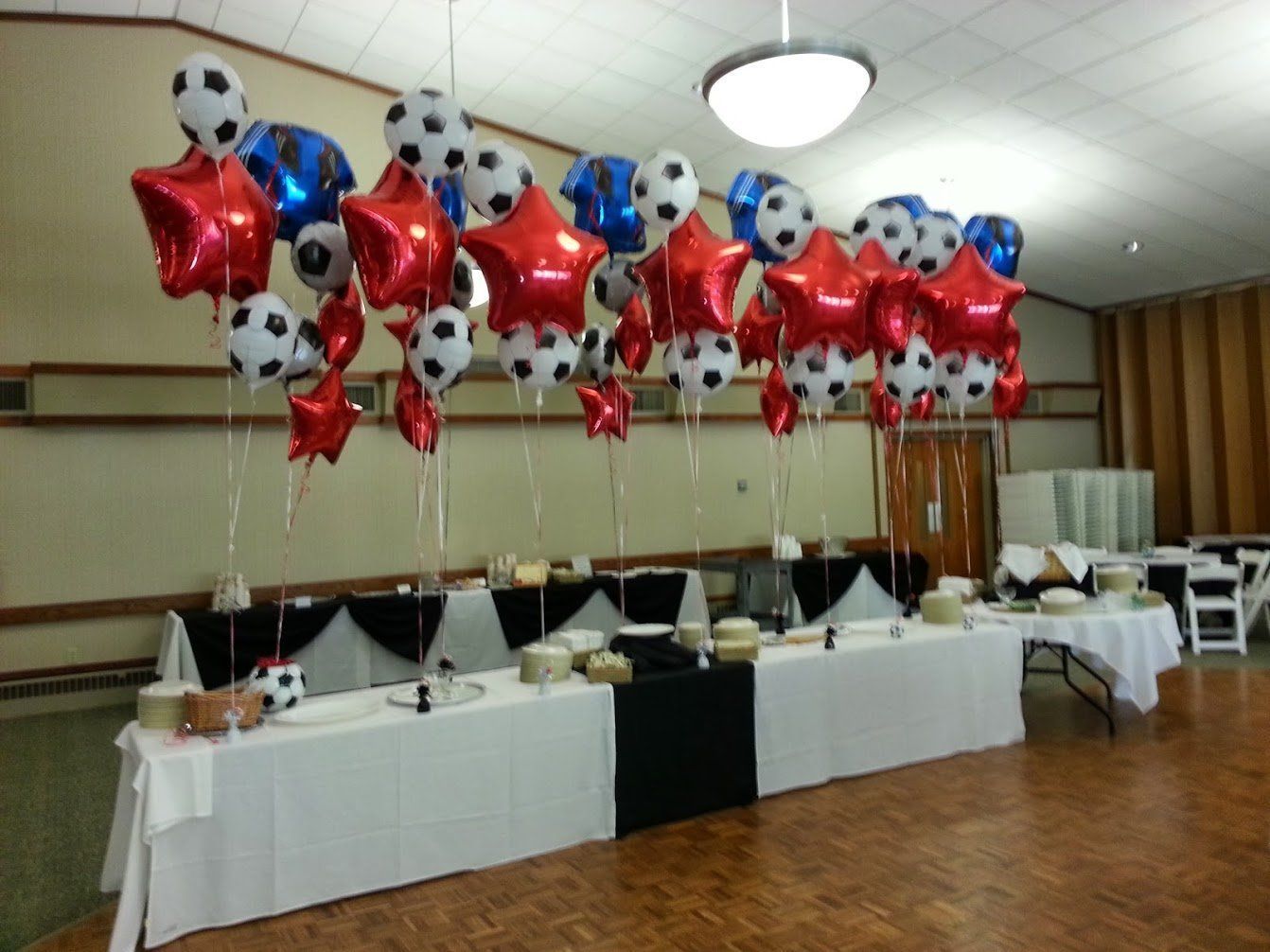 Balloon-decorated banquet table with red star balloons and soccer ball balloons in a reception hall