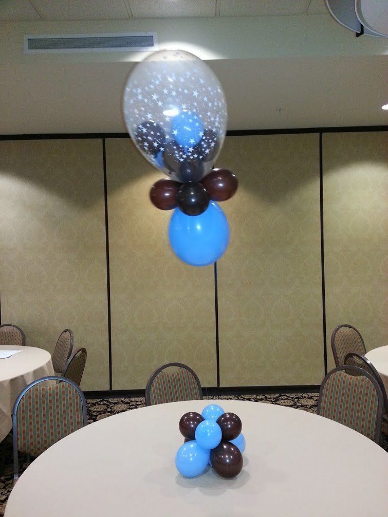 Balloon centerpieces in a banquet room, with blue, brown, and clear balloons on round tables.