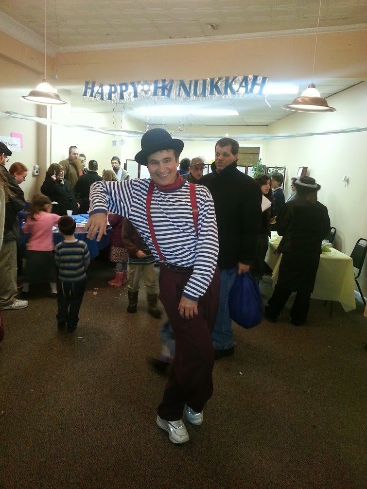 Man in striped shirt and bowler hat dancing at a lively indoor party with streamers and guests