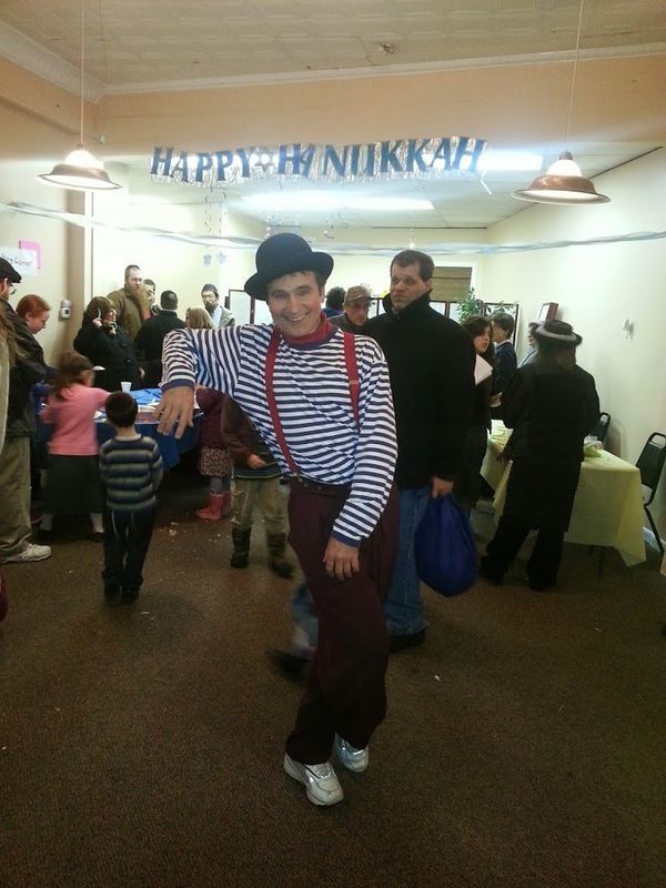 Person in striped shirt and red suspenders dancing at a lively Hanukkah party indoors.