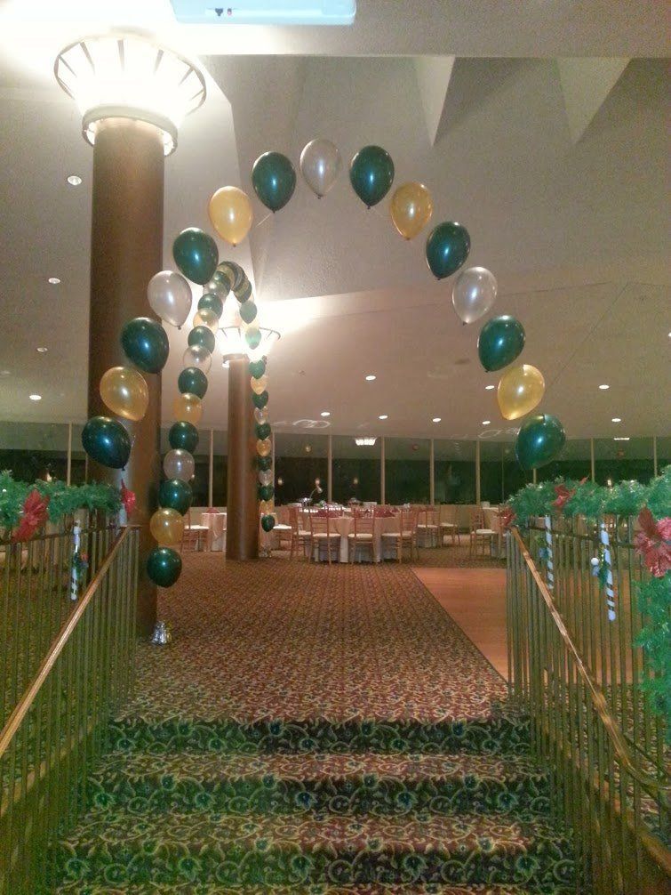 Balloon-decorated entrance walkway with archway, green carpet, and banquet hall tables in the background