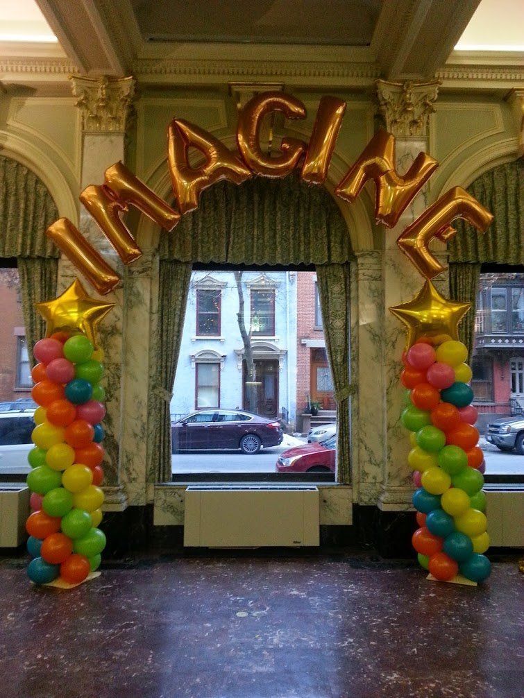 Colorful balloon arch spelling “IMAGINE” in a hall with a window view outside