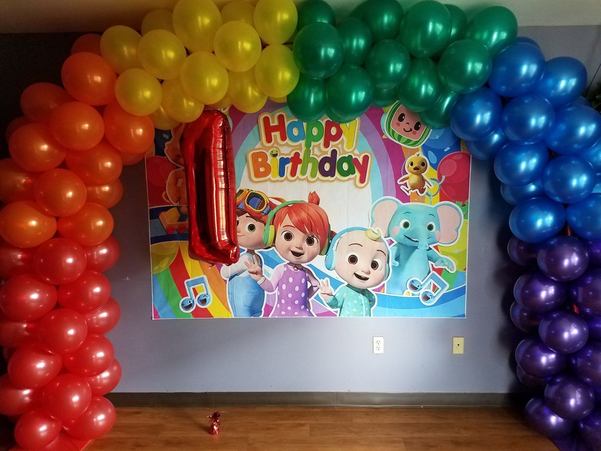 Rainbow balloon arch framing a “Happy Birthday” banner with cartoon characters on a wall.