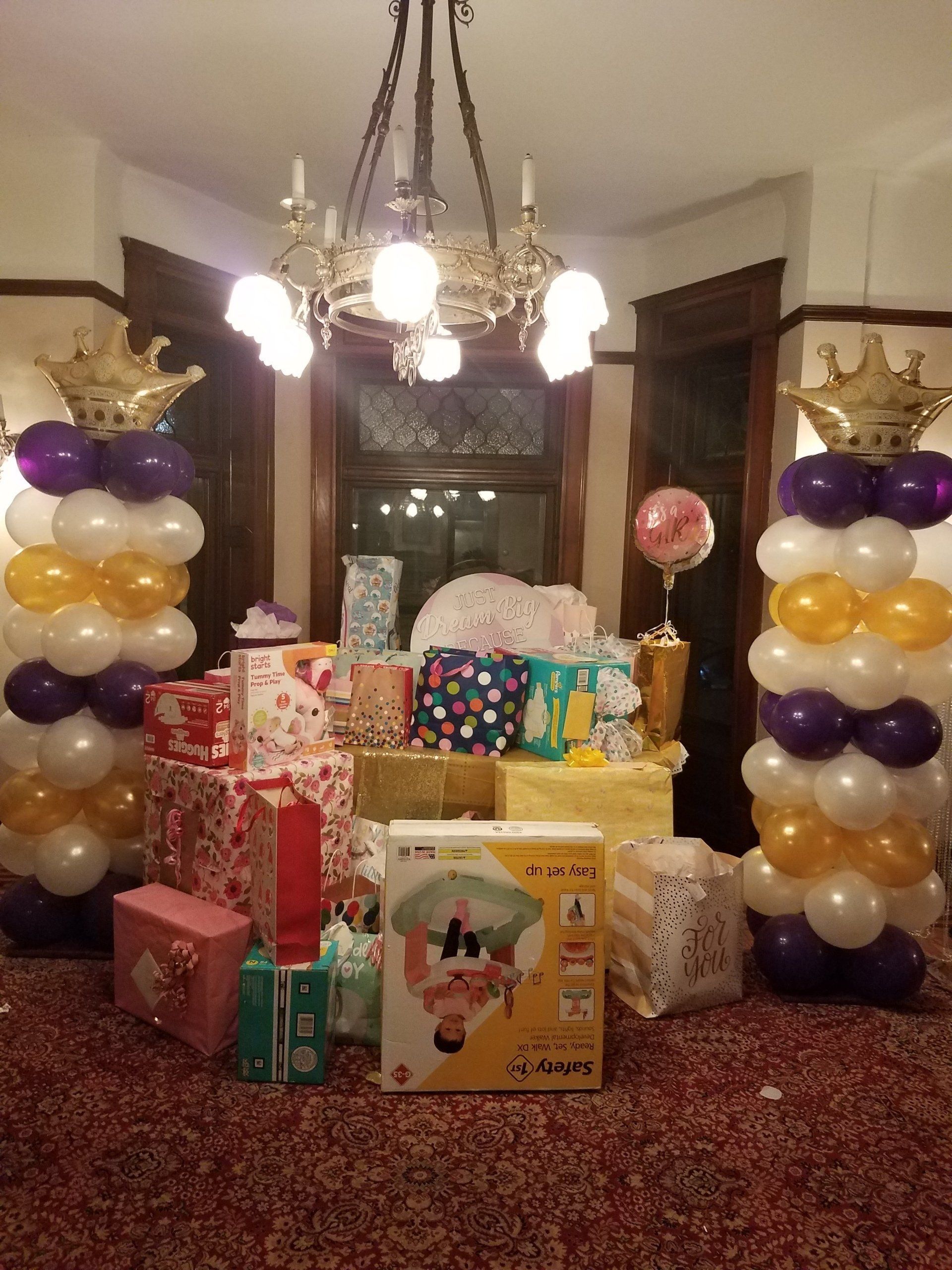 Living room decorated with balloon towers and a chandelier, with many wrapped gifts and boxes on the floor.