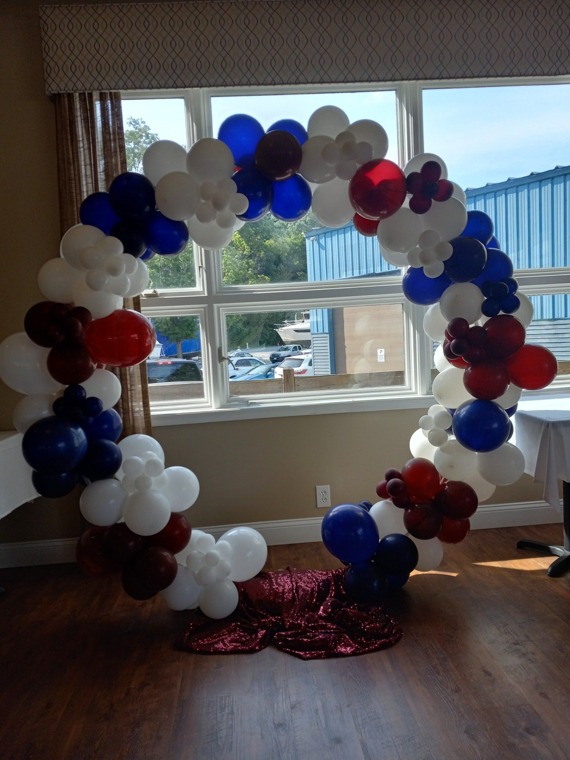 Red, white, and blue balloon arch around a window with a red sequin floor decoration