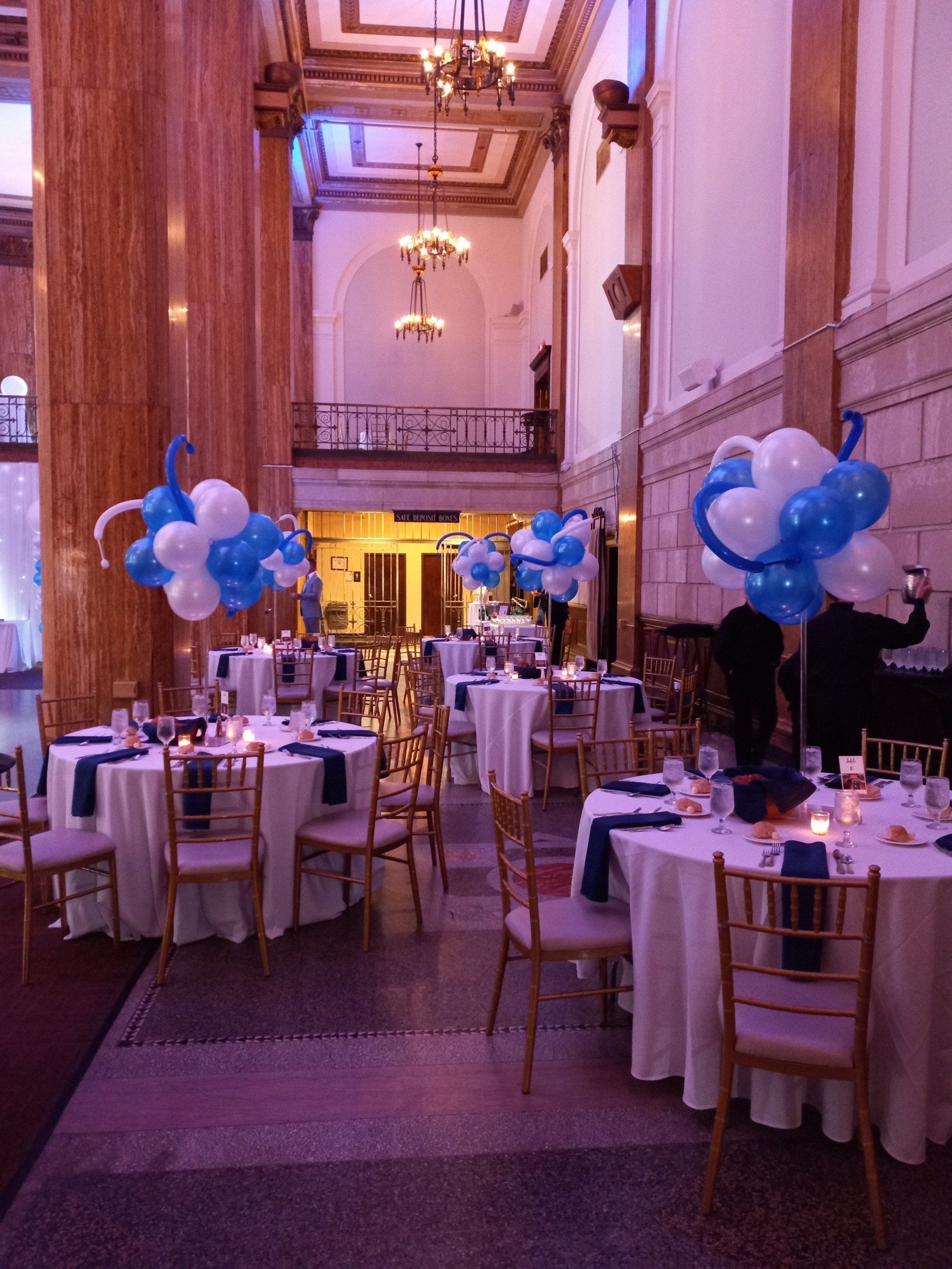 Decorated banquet hall with blue balloon centerpieces and round tables set for an event