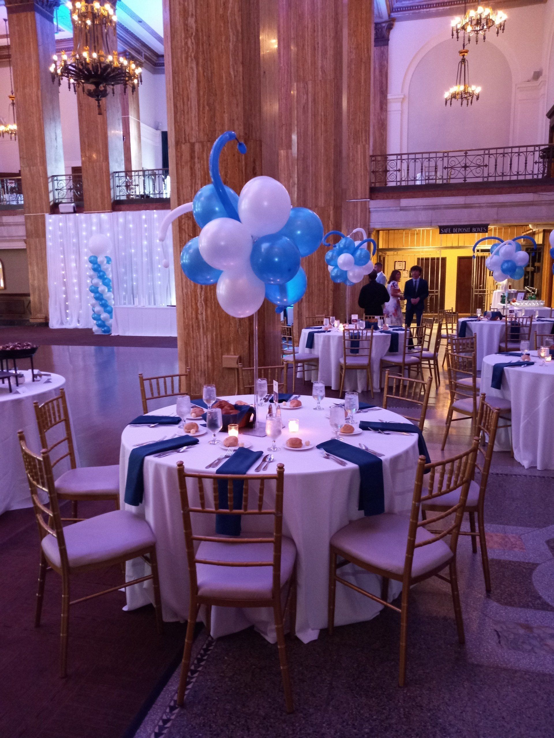 Elegant banquet hall with round tables, gold chairs, and blue-and-white balloon centerpieces