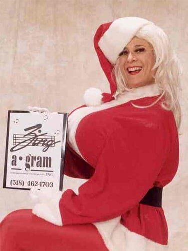 Woman in a red Santa outfit holding a sign against a plain background.