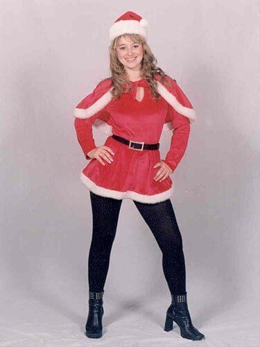 Person in a red-and-white Santa outfit and hat, posing with hands on hips against a plain gray background