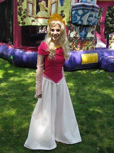 Woman in a pink dress and white skirt standing in front of a colorful inflatable bounce house outdoors