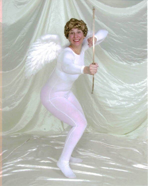 Person in white costume with angel wings, holding a prop and posing against a draped white backdrop.
