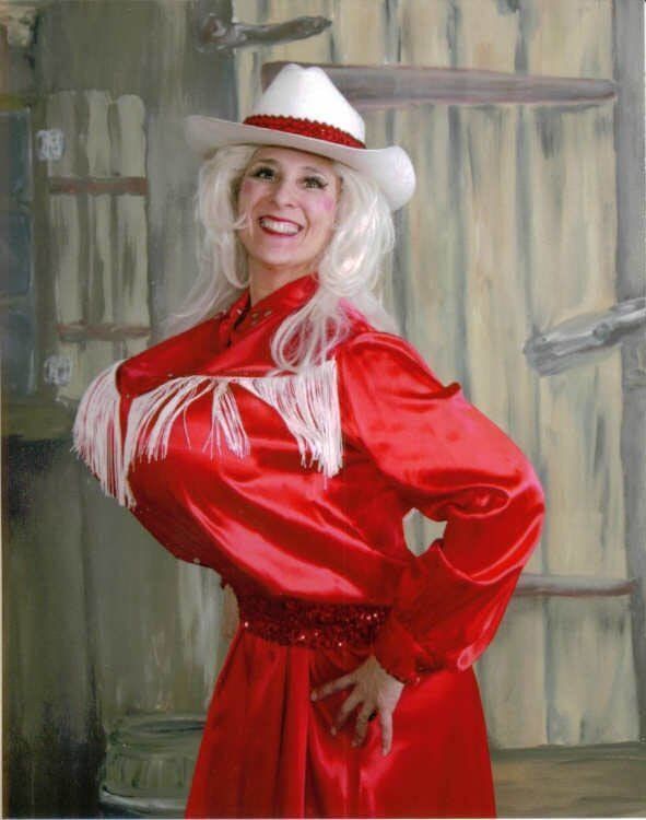 Woman in a red dress and white cowboy hat smiling with hands on hips against a painted backdrop