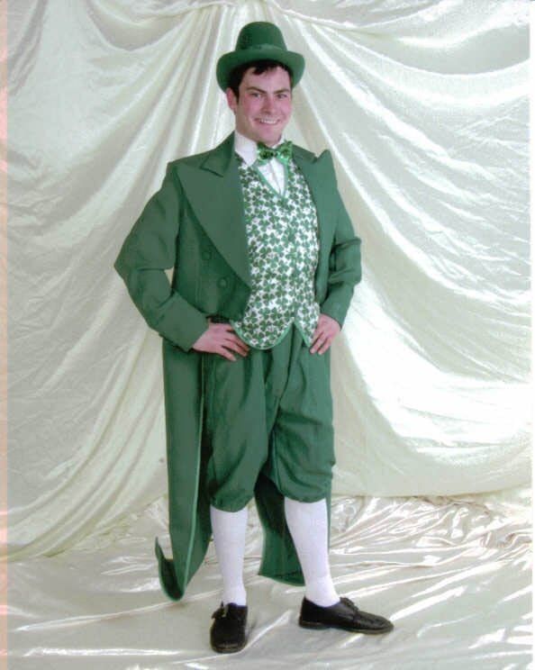 Person in a green suit, top hat, and vest posing with hands on hips against a draped white backdrop.