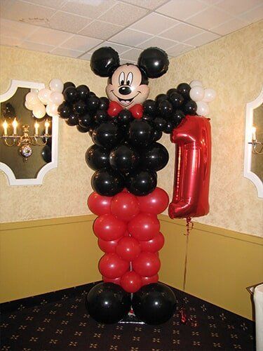 Mickey Mouse balloon sculpture in red, black, and white, standing indoors at a party