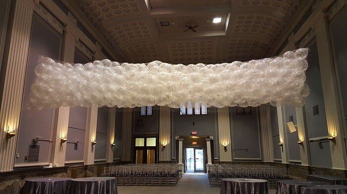 Large white balloon cloud installation hanging across a grand indoor hall with chandeliers and tables below