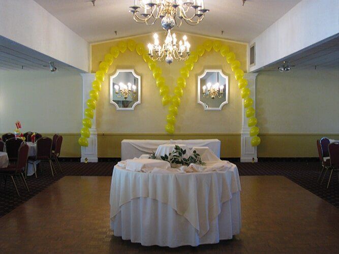 Decorated banquet hall with yellow balloon arch, chandelier, and round table with white tablecloth