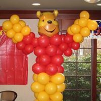 Winnie the Pooh balloon sculpture with red shirt and yellow pants, arms raised indoors